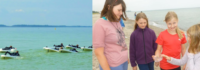 Surfer im Wasser und Kinder begutachten Muscheln