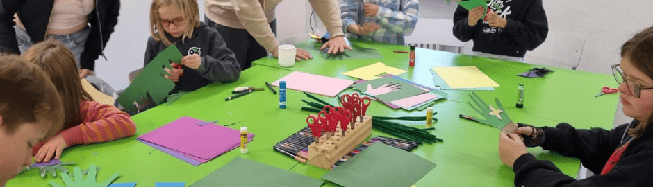 Kinder die an einem Tisch sitzen und mit buntem Papier basteln