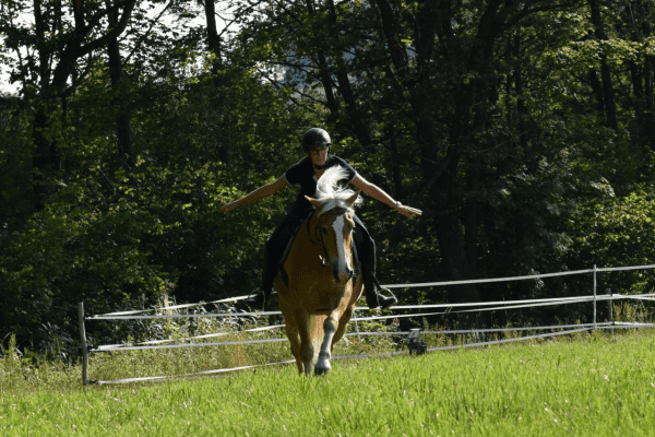 Frau reitet freihändig über eine Wiese