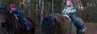 Zwei Mädchen beim Reiten am Waldrand