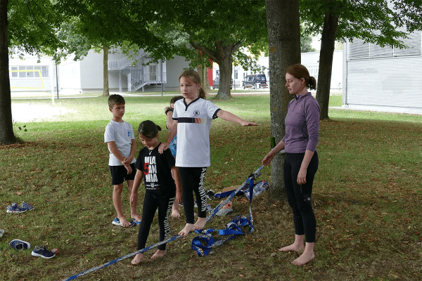 Mädchen balanciert mit Hilfe auf einer Slackline