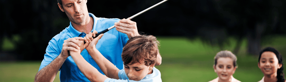 Erwachsener erklärt Golfschlägerhaltung, während andere Kinder zuschauen