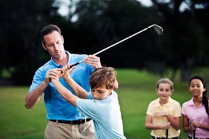 Junge bekommt Hilfe bei der Technik vom Golflehrer