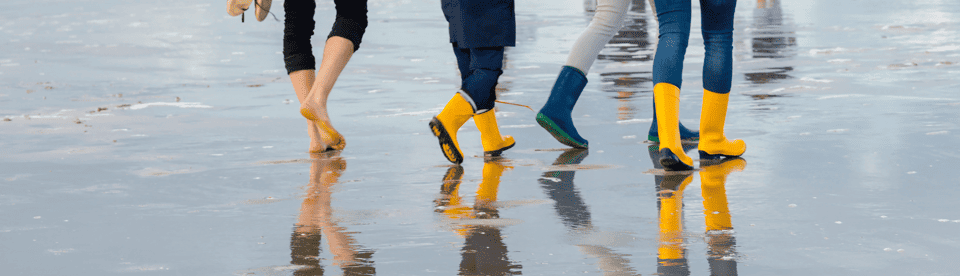 Kinder laufen am Strand barfuß und mit Gummistiefeln