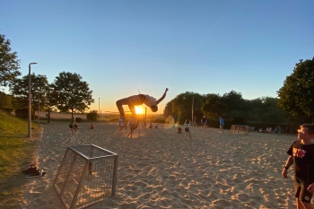 Ein Jugendlicher beim Rückwärtssalto im Sand beim Sonnenuntergang am Strand.