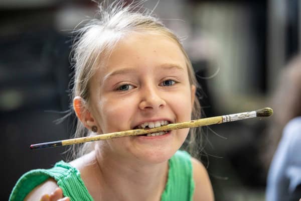 Clavis Schule Kunstcamp Kind hat einen Pinsel im Mund