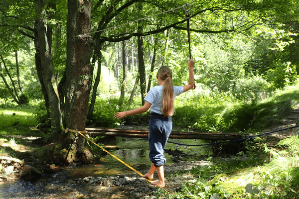 Kind balanciert in der Waldfreizeit Thüringen über einen Bachlauf