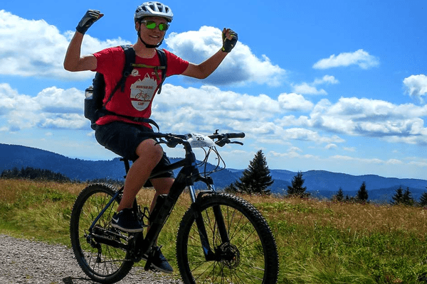 Mountainbiker fährt durch Natur und hält beide arme hoch