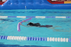 Kind schwimmt mit Poolnudel im Schwimmcamp