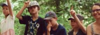 Kinder sitzen im Wald auf einem Baumstamm