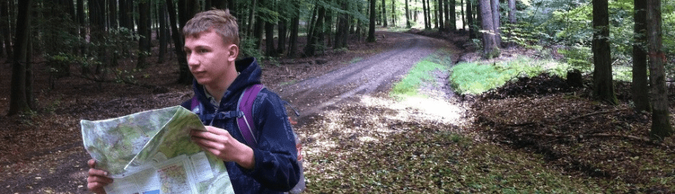 Ein Junge mit einer Landkarte auf einem Waldweg