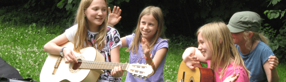 Gruppe von Mädchen beim Singen mit Gitarre