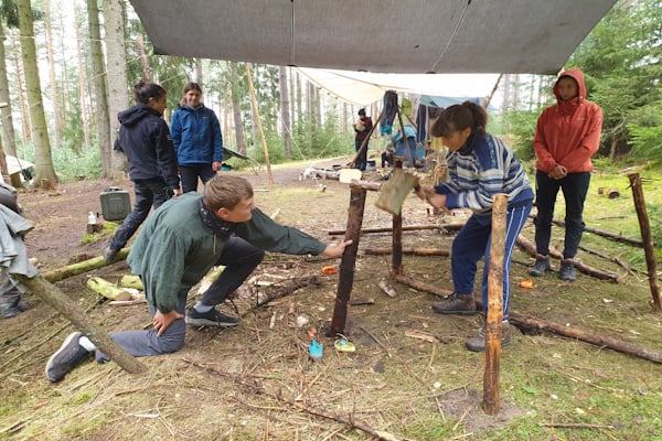 Jugendliche die unter einer Plane im Wald etwas bauen