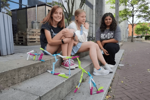 Drei Mädchen sitzen draußen auf Treppe, Projektarbeit - Konstrukt aus Wäscheklammern