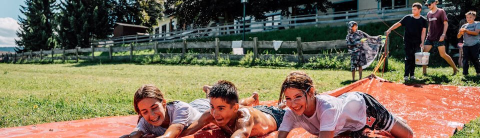 Kinder lachend auf Wasserrutsche auf der WIese