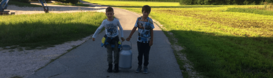 Zwei Jungen tragen große Milchkanne