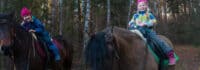 Zwei Kinder reiten im Wald