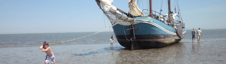 Junge zieht Segelschiff übers Watt