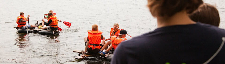 Kinder fahren mit ihren selbstgebauten Floßen auf dem Wasser