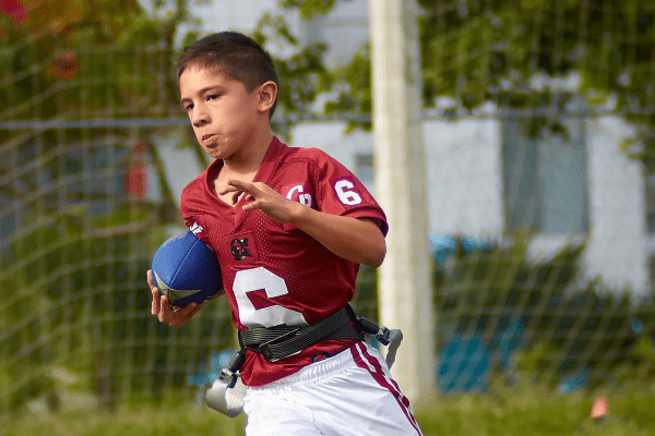 Junge rennt mit Rugby im Englisch & Sport Camp im Grünen