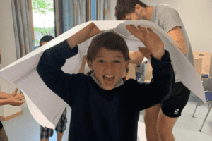 Junge lacht unter Papier im Englisch Camp Salzburger Land