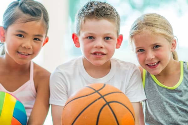 drei Kinder sitzen neben einander und haben einen Basketball in der Hand