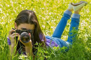 Mädchen liegt mit Kamera auf einer Wiese