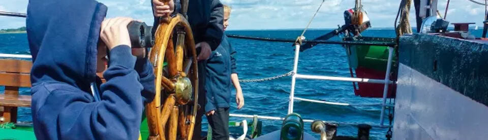 Junge am Steuerboard schaut durchs Fernglass aufs Meer