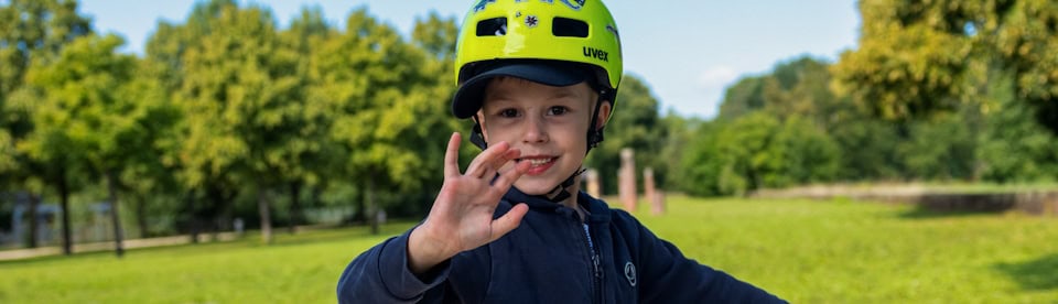 Ein Junge mit Fahrradhelm winkt in die Kamera