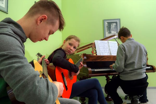 Ein Kind am Klavier und zwei Kinder mit Gitarre im Klavier Camp Schloss Leizen