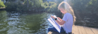 ein Mädchen sitzt mit einem Buch am See