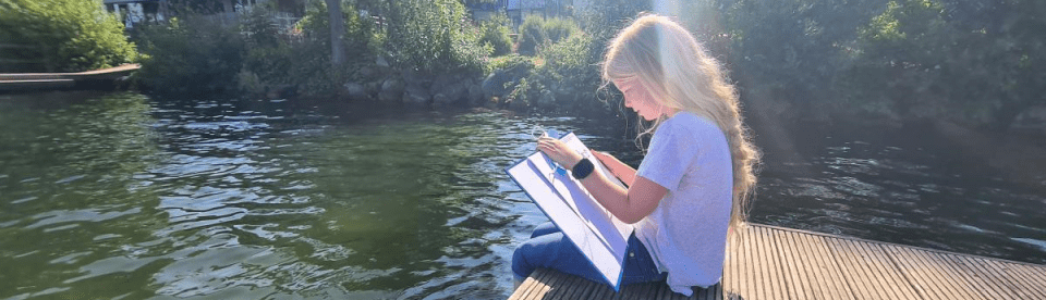 ein Mädchen sitzt mit einem Buch am See